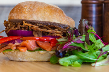 Close up shot of Salmon gravlax sandwich and onion duo, with leafy vegetables on side, blurred saltshakers can be seen as well