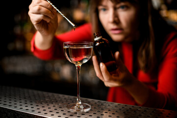 close-up of glass with liquid in which woman accurate adds the ingredient drop by drop