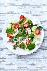 Healthy Salad with Feta Cheese, Green Olives, Baby Spinach, Cucumber, Cherry Tomatoes and Capers. Bright wooden background. Top view.