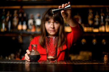 glass stands on bar and female bartender carefully pours drink from jigger into it