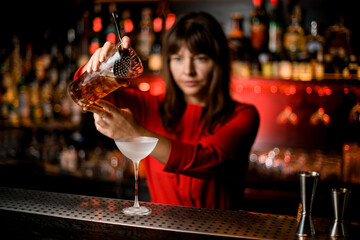 wineglass stands on bar and woman bartender holds mixing cup with cold drink over it