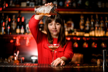 front view on wineglass standing on bar and bartender holding mixing cup and accurate pours drink into it