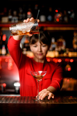 wineglass stands on bar and barkeeper holds mixing cup and skilfully pours drink into it
