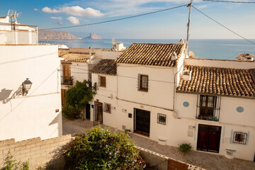 Beautiful narrow street in the old town with white houses and tiled roofs, on the horizon the sea and rocks, the old town of Altea, Spain.