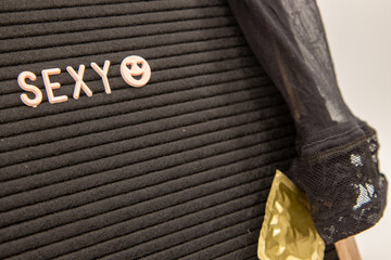 A black board saying the word sexy draped over with a sexy stocking and a gold condom