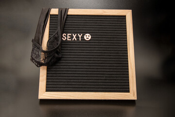 A black board saying the word sexy draped over with a pair of sexy black panties