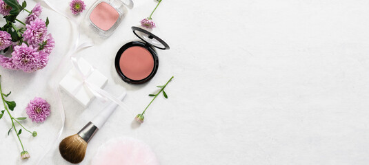 Beautiful festive composition with fresh aromatic flowers, make up brushes, present boxes, bags and decorative cosmetic products on white marble background long banner format.