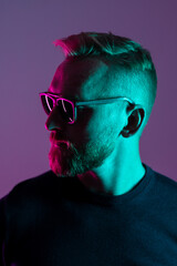 Portrait of a macho man wearing sunglasses looking away from camera. Close up shot with neon...
