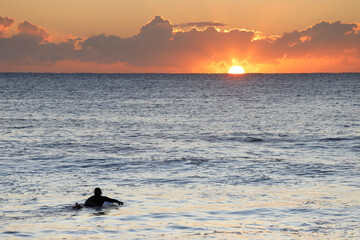 Naklejka na ściany i meble Surfer paddling on the ocean at sunrise.