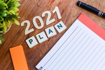 View from above of block letters on the plan and number 2021 with an empty notebook, a pen, and label tag on the wooden table 
