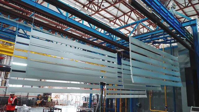 Silver metal panels move on an overhead conveyor. Powder coating line