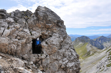Człowiek stoi w skalnym otworze na szczycie góry podczas wspinaczki na via ferrata, Dolomity - obrazy, fototapety, plakaty