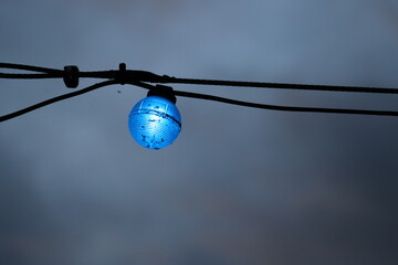 Single bright blue colored light bulb against a dark sky.