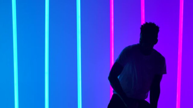 A dancer performs a dance element from a salsa program in slow motion. Silhouette of men against the background of multicolored neon lights in the studio. Close up.