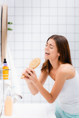 excited young woman singing with hairbrush in bathroom