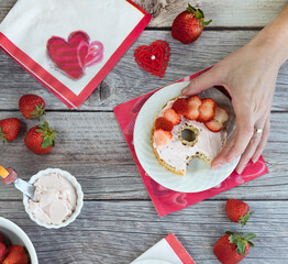 Above view of a cream cheese and strawberry covered bagel with a hand taking it off the plate. Valentine's Day concept.