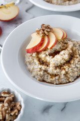 Close up of a bowl of steel cut oats and brown sugar with apple slices and walnuts ready for eating.