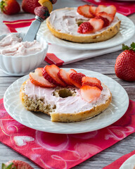 Bagel with a bite out covered in strawberry cream cheese and sliced strawberries ready for eating.