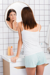smiling woman in white singlet standing in bathroom and looking in mirror