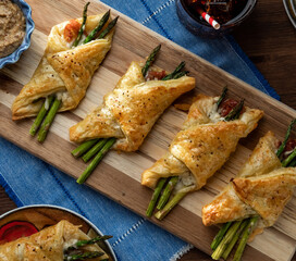 Close up of asparagus and prosciutto pastry bundles against a dark background with sunlight streaming in.