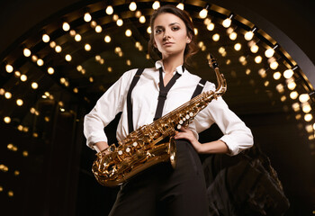 Gorgeous brunette model woman in fashionable formal suit with saxophone