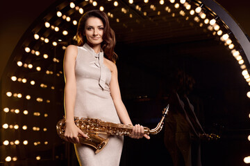 Gorgeous brunette model woman in elegant dress with saxophone