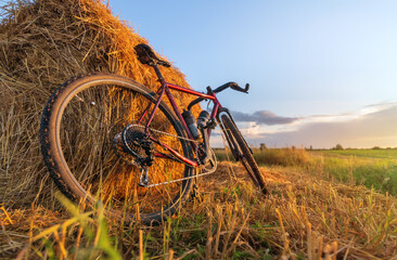 Naklejka premium Bicycle stands by haystack in a field at sunset. Low angle view.