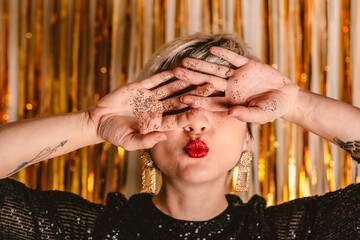 Young millennial blonde woman celebrating New Years Eve. Glitter sparkling confetti. Cocktail party night. Having fun. Golden wall. red lips. Luxury dress. White black. Happy Birthday. Smiling person
