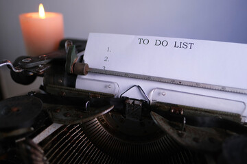old typewriter on table, words to do list are printed on paper in large size, candle is burning,...