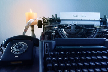 old typewriter on table, words fake news are printed on paper in large size, candle is burning,...