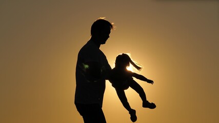 Fototapeta na wymiar Dad day silhouette with daughter at sunset. The daughter flies in the arms of her father with her arms out to the sides. The girl soars in the sky in the arms of her beloved parent. Separation from
