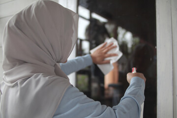 Muslim woman cleaning window glass with wag and spray