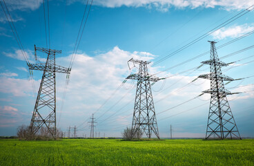 High voltage lines and power pylons in a flat and green agricultural landscape on a sunny day with...