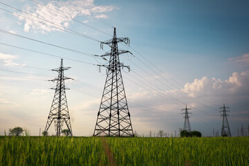 High voltage lines and power pylons in a flat and green agricultural landscape on a sunny day with...