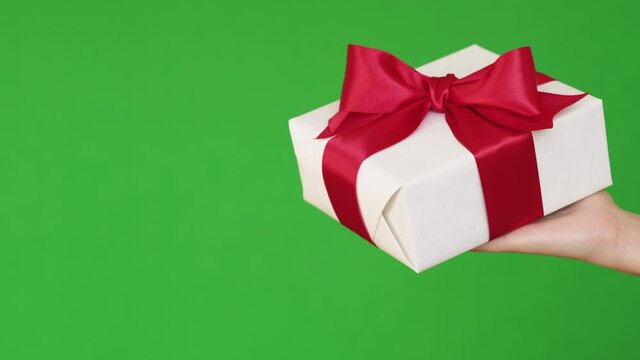 Holiday surprise. Women day gift. Festive occasion greeting. Special offer. Female hand showing present in white wrapped box with red ribbon bow isolated on green empty space background loop.