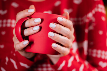 Woman in ugly sweater holding cozy red mug on Christmas tree background. Girl with hot drink - tea, coffee or cocoa. Concept of the New Year, comfort and warmth.