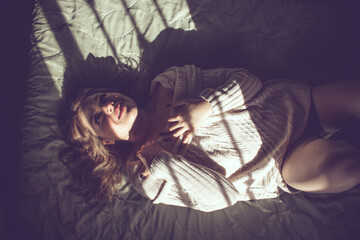 beautiful happy woman with sensual lips lying on the bed with light coming through the window