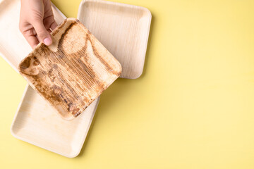 Hand holding betal palm leaf plate (Biodegradable, Compostable, Disposable or Eco friendly plate) on yellow background, Sustainable concept
