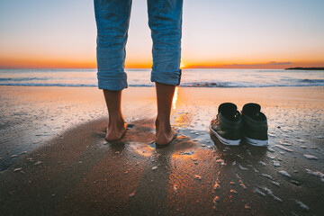 Closeup of barefoot man walking on the summer beach at sunset. Man take off his shoes for walk in...