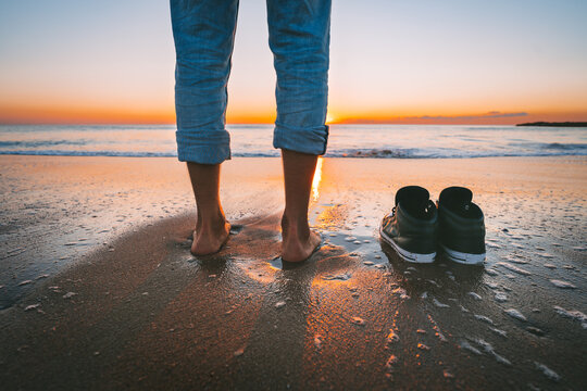Closeup of barefoot man walking on the summer beach at sunset. Man take off his shoes for walk in the calm sea. Relaxation and freedom concept.