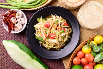 Thai food (Som tum), Spicy green papaya salad with vegetables on woven bamboo background, Top view