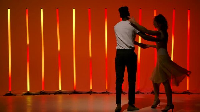 A beautiful sensual couple perform passionate dance steps of Hispanics against a bright red orange neon background. A man and a woman are dancing salsa in slow motion.
