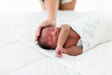 African American newborn baby sleeping and holding mother’s finder on white bed. Happy family mother and her newborn