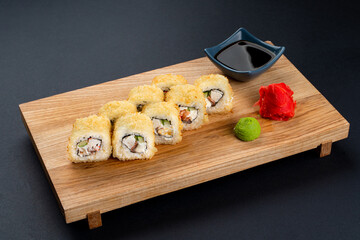 Full set of warm deep fried sushi rolls with fresh fish and cream cheese on a wooden plate, black background shot