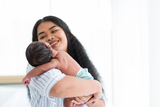 Newborn baby or infant sleeping on mother shoulder. Happy African American mum holding comforting her baby at home