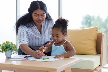 Happy African American mother and her little daughter. Mother teaching her daughter drawing and...