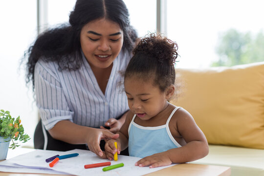 Happy African American mother and her little daughter. Mother teaching her daughter drawing and painting. Mom spending time with her daughter. Happy family at home