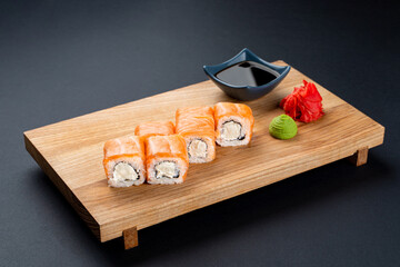 Philadelphia sushi rolls with cream cheese and raw salmon slices in soft studio light on black background