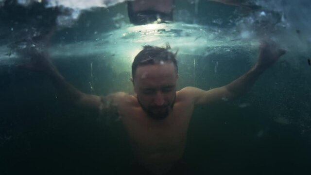 Winter swim. Young man swims in the winter lake. Splitted footage with underwater view of the icy water