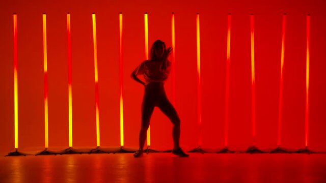 A solo performance by a professional dancer in the studio against the background of multicolored neon lights. Young woman dancing salsa passionately, moving her hips in slow motion.